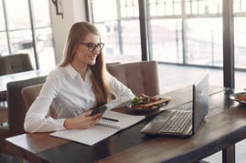 young-cheerful-businesswoman-using-smartphone-and-laptop-in-3874627